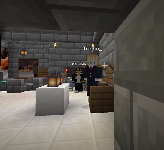 This is a screenshot from Tommy's stream. He stands in a jail cell, looking at the court before him. Tubbo sits at the judge's stand while Fundy stands at attention at the levers as executioner. Should they find Tommy guilty, they would drop Tommy into the lava below. The room is built with stone brick and lit up by lanterns. There are a few paintings on the walls.